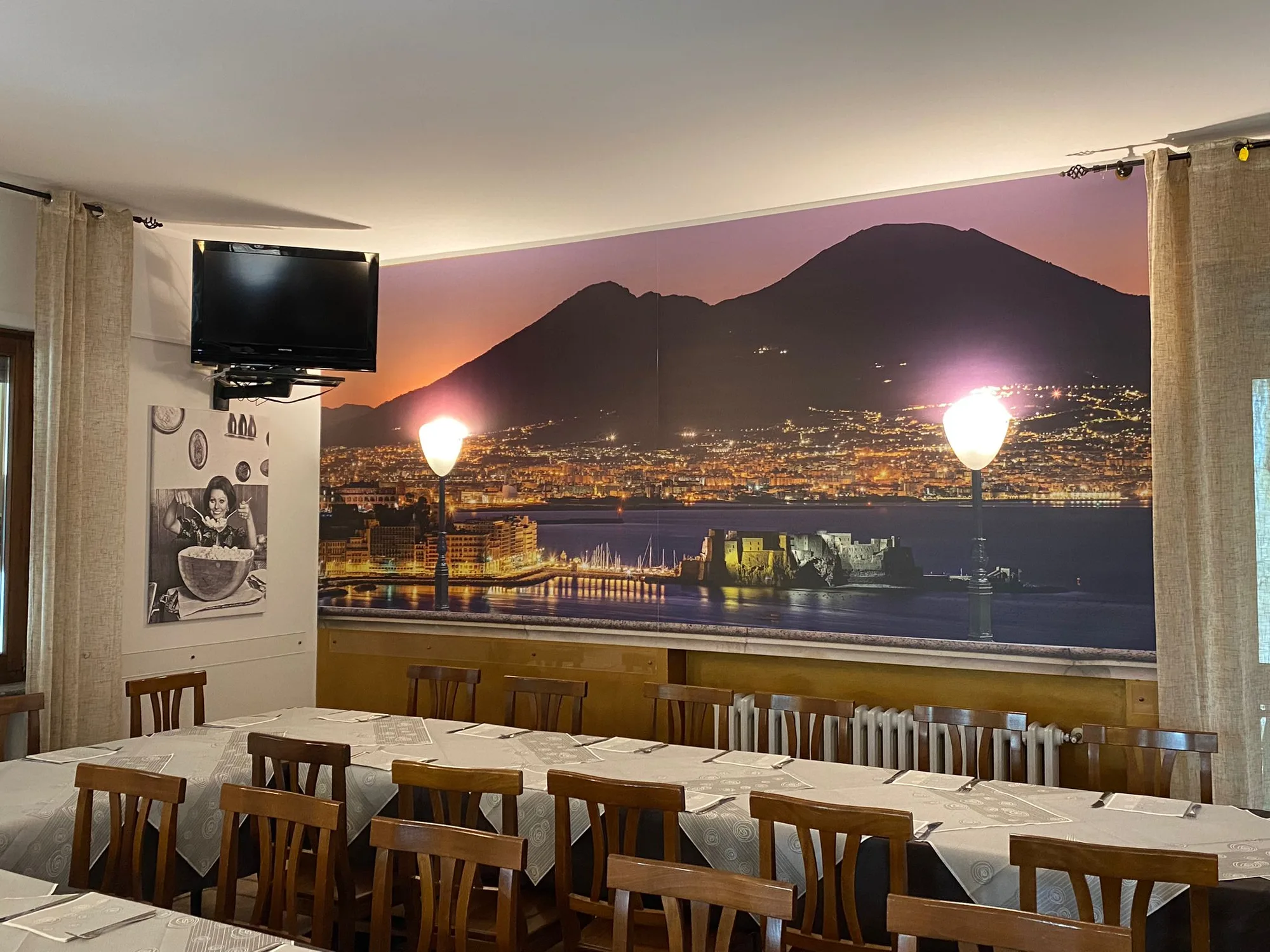 Sala di un ristorante con parete rivestita da pannelli stampati con il golfo di Napoli e il Vesuvio di sera