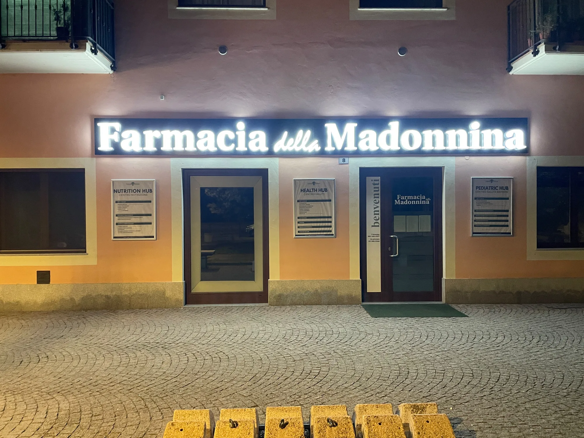Insegna a lettere luminose bianche sulla facciata di una farmacia, di sera