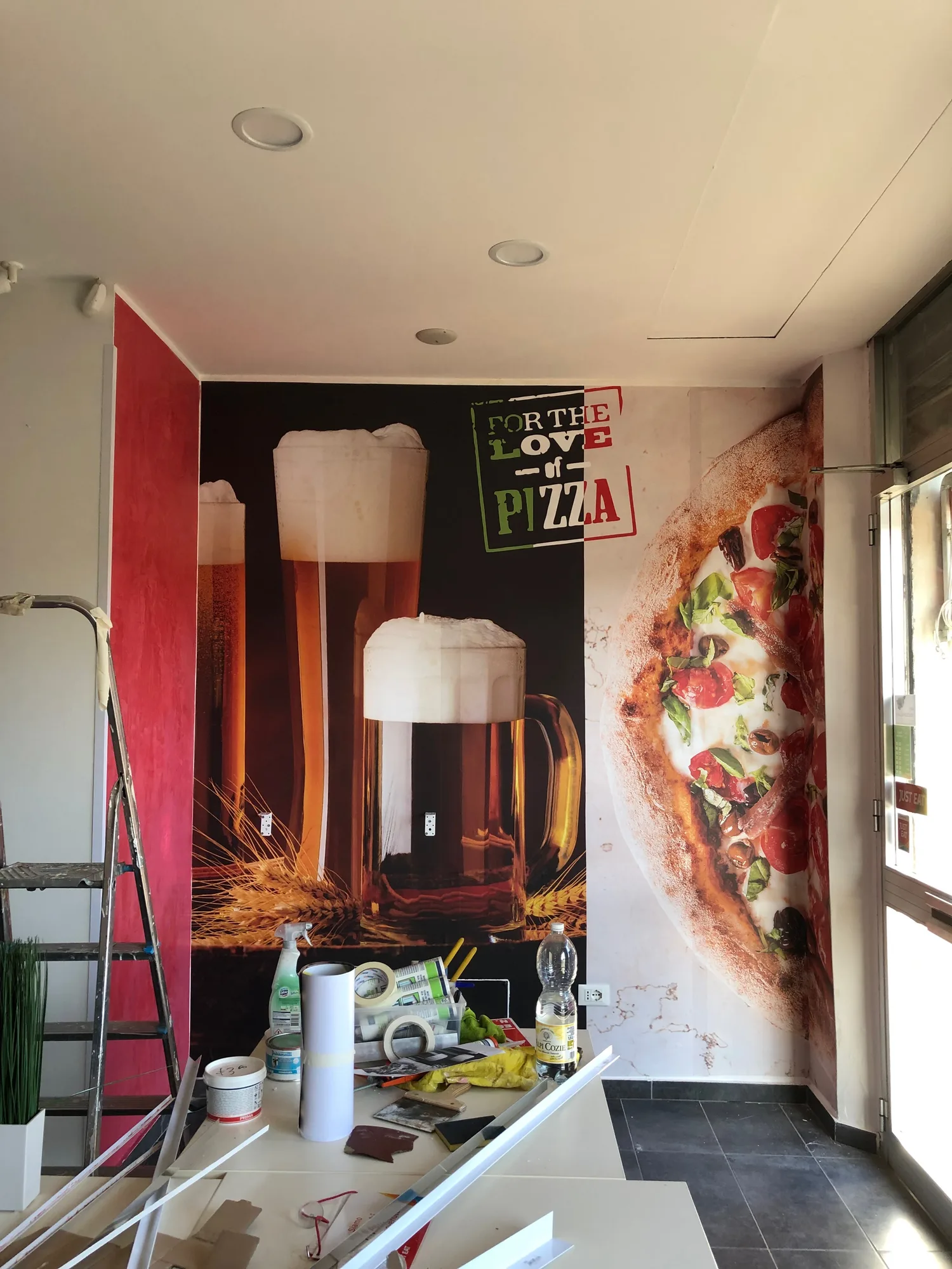 Parete di una pizzeria rivestita con grafica di boccali di birra e pizza durante la posa