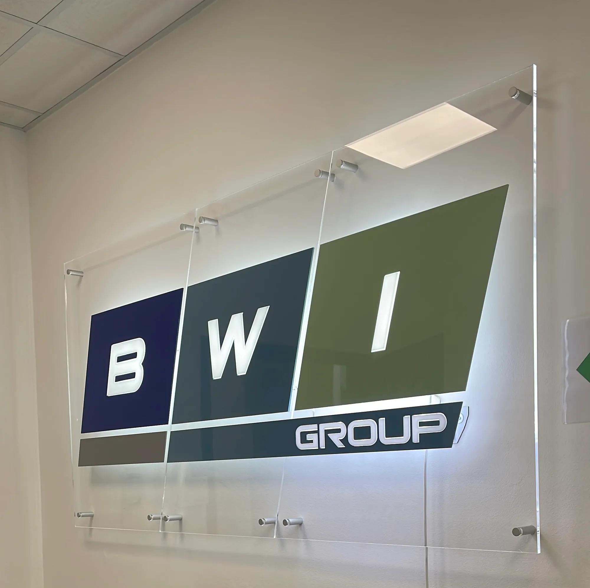 Logo aziendale su pannello in plexiglass a più strati, illuminato da dietro e fissato a parete con distanziali