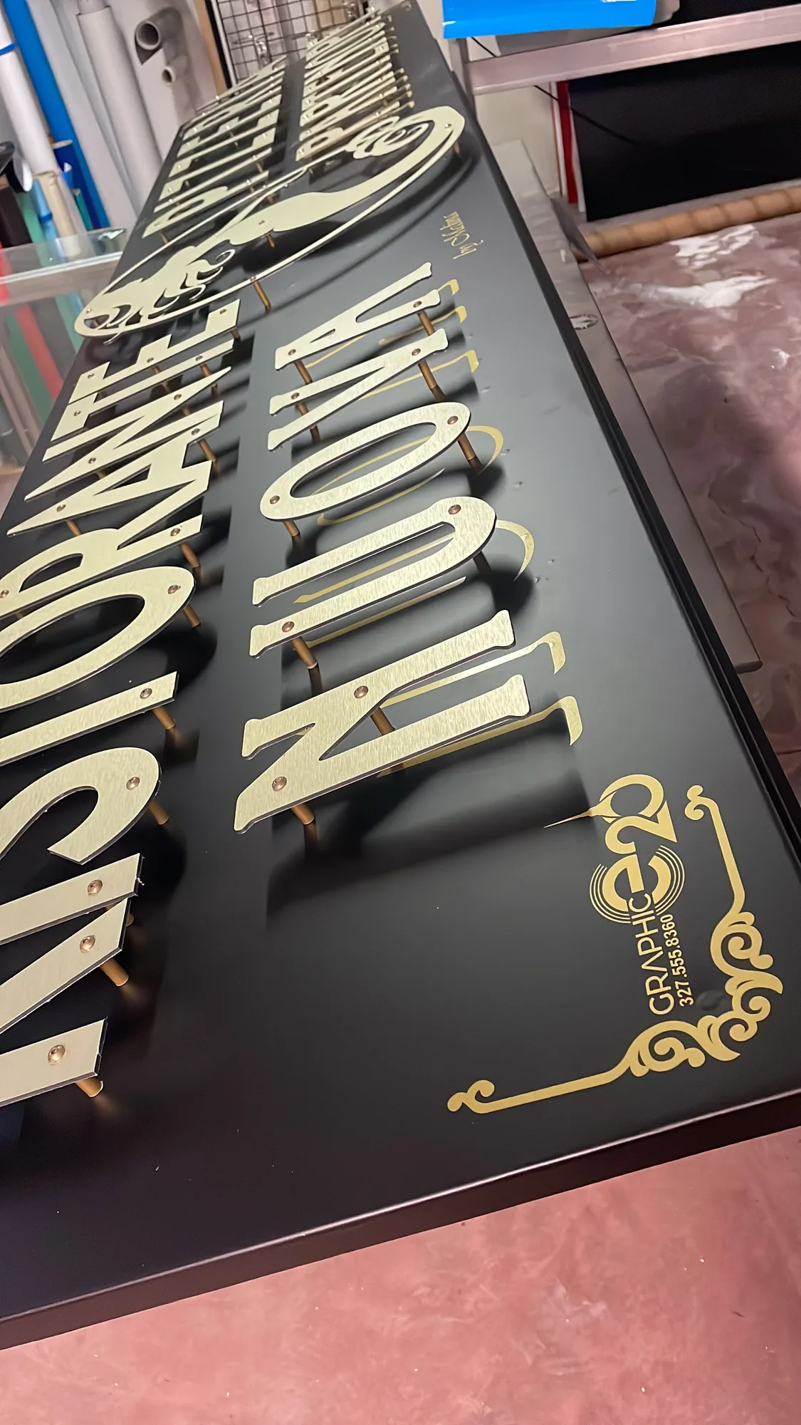 Insegna nera con lettere in rilievo color oro distanziate dal fondo, in lavorazione in laboratorio
