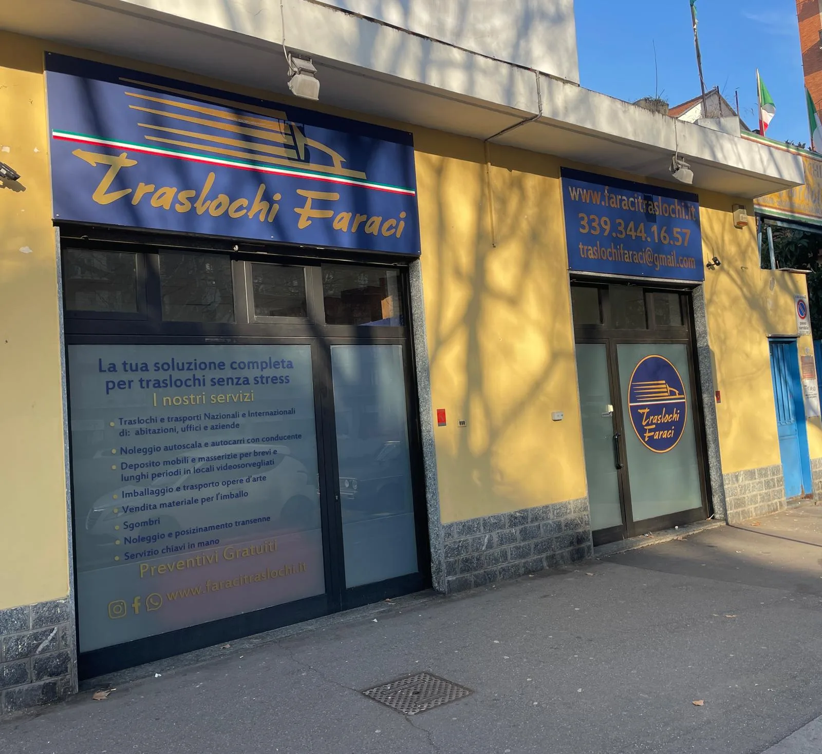 Insegna blu e oro e vetrofanie con l'elenco dei servizi sulla facciata di un'impresa di traslochi