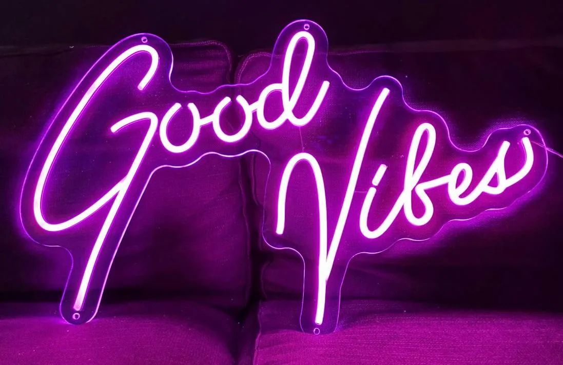 Scritta Good Vibes in neon led viola su pannello trasparente, appoggiata su un divano