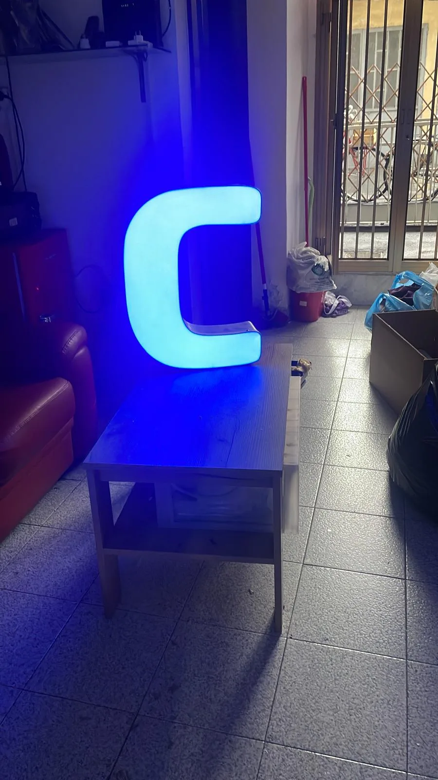 Lettera C luminosa azzurra appoggiata su un tavolino come lampada d'arredo