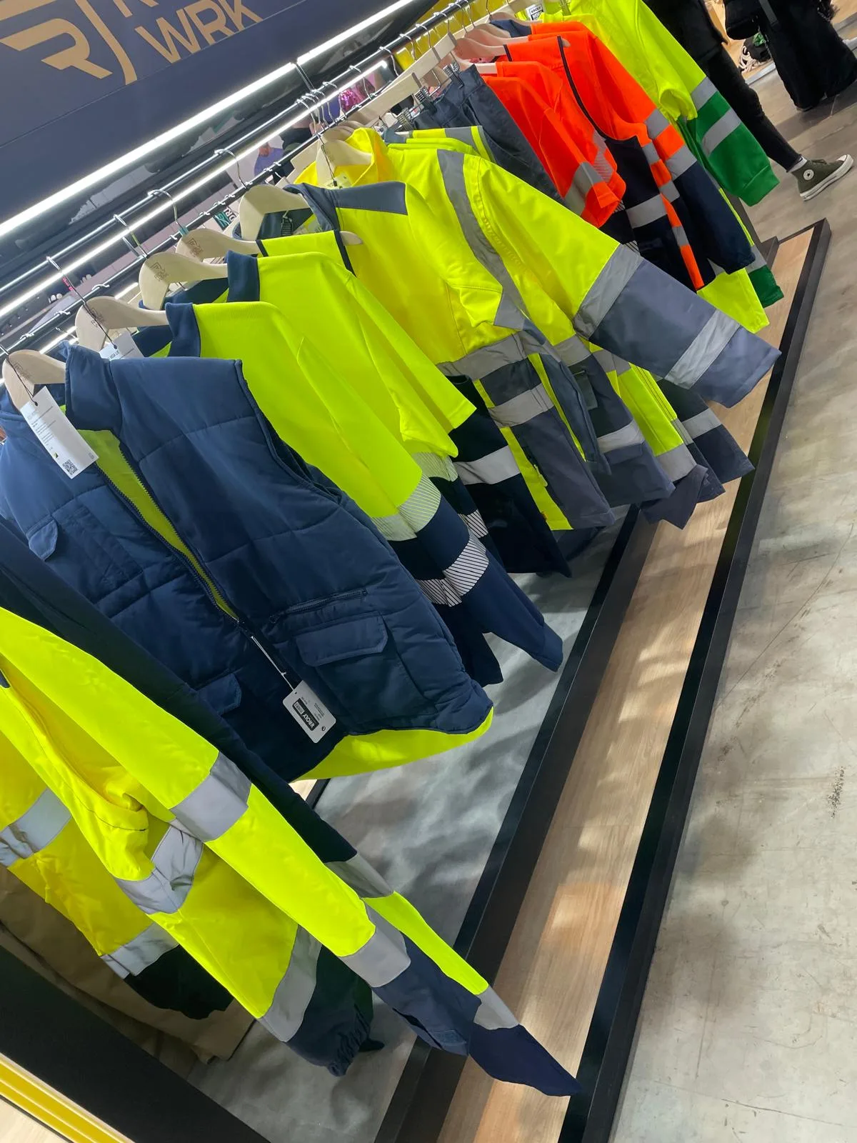 Fila di giacche e gilet da lavoro ad alta visibilità gialli, arancioni e blu appesi in esposizione