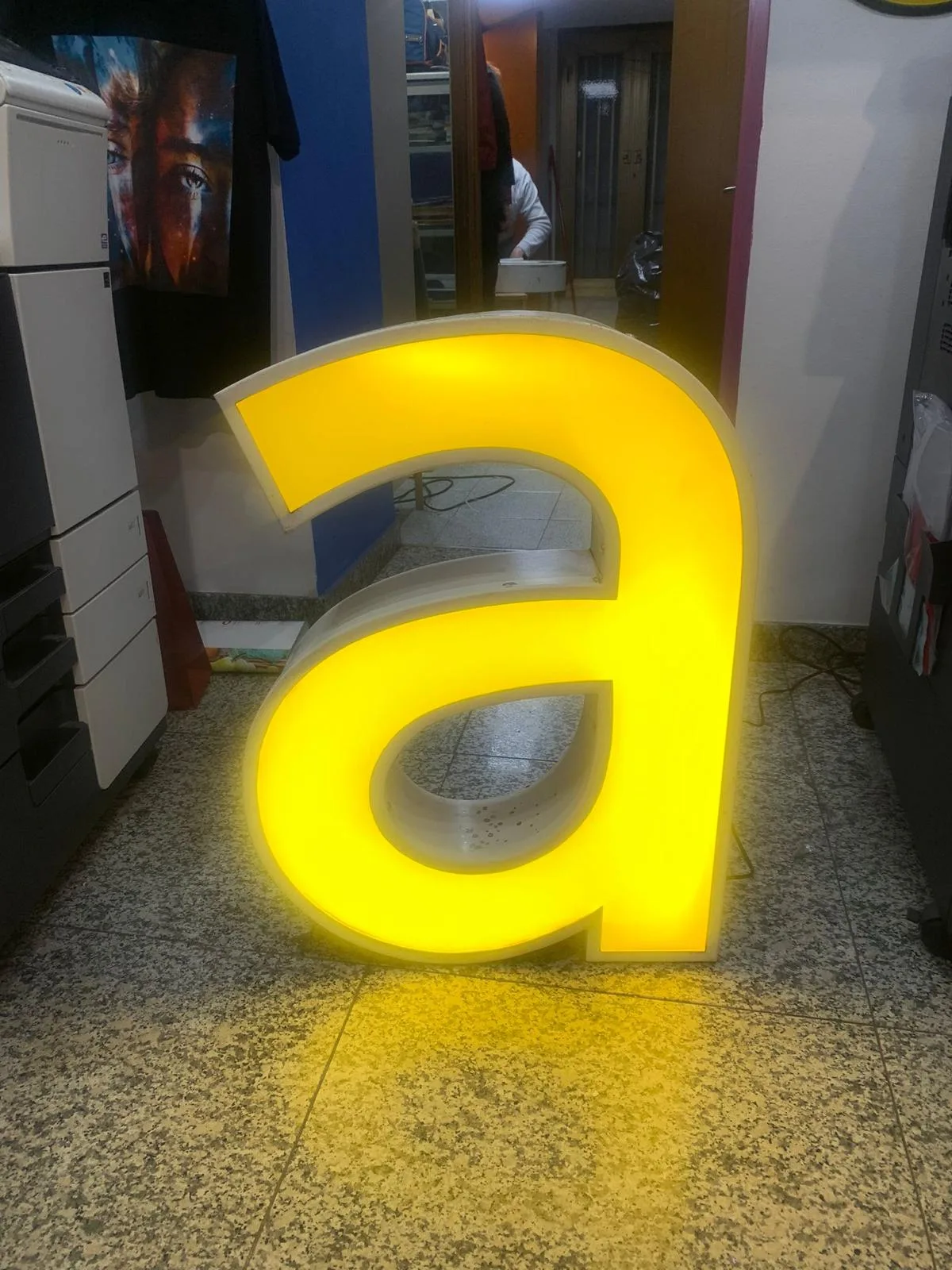 Grande lettera a minuscola luminosa gialla recuperata da una vecchia insegna, accesa in negozio