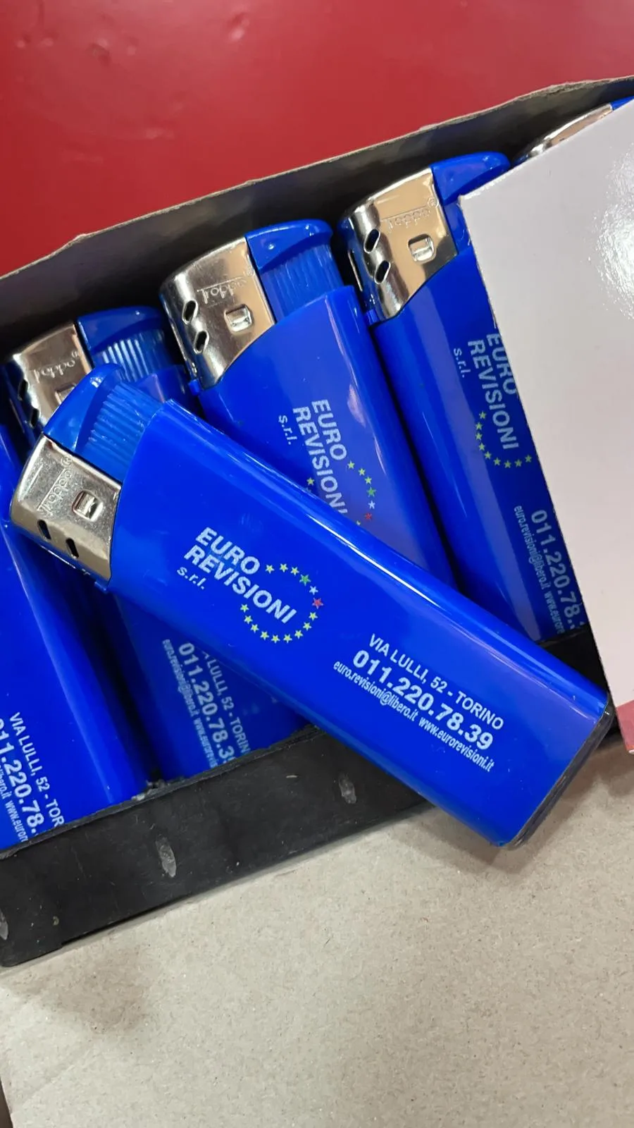 Accendini blu personalizzati con logo, indirizzo e telefono di un'azienda di revisioni auto, nella loro scatola