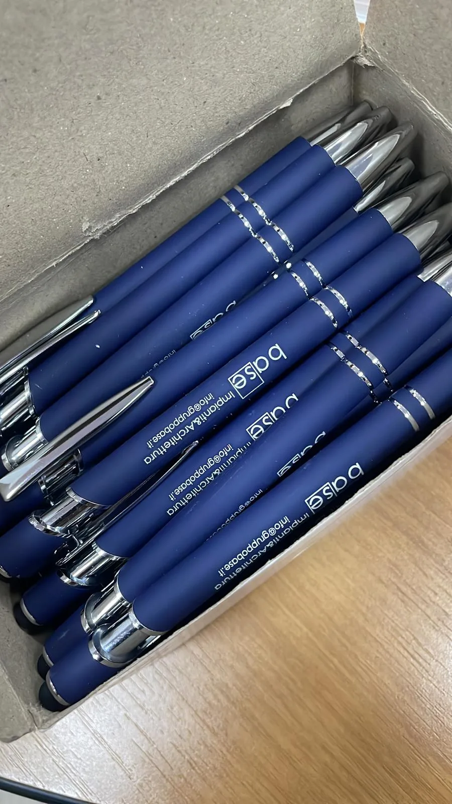 Scatola di penne blu opache con logo e contatti di uno studio di impianti e architettura incisi in argento