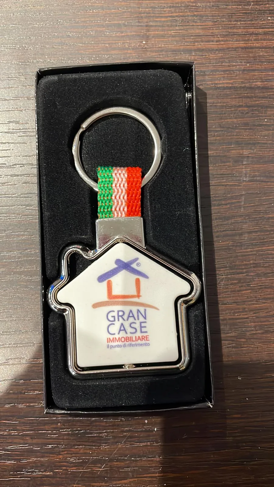Portachiavi a forma di casa con logo di un'agenzia immobiliare e fettuccia tricolore, nella confezione regalo
